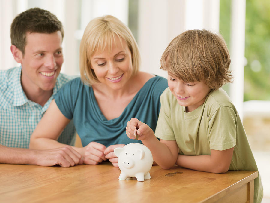 Parents watching son putting coin into piggy bank Photograph by Chris Ryan