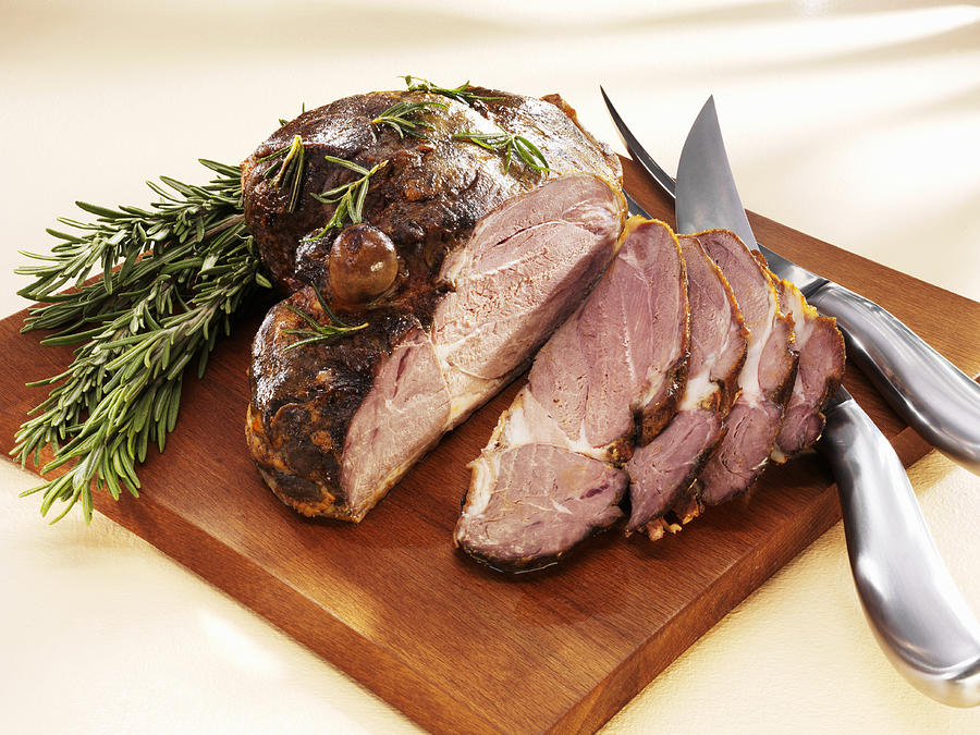 Partially sliced roast leg of lamb on chopping board Photograph by Foodcollection RF