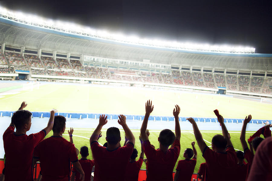Passionate fans cheer and raise hands at a sporting event in the stadium Photograph by Shannon Fagan