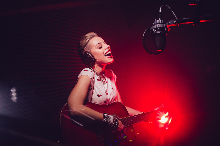 Passionate singer playing the guitar and recording song in studio Photograph by Wundervisuals