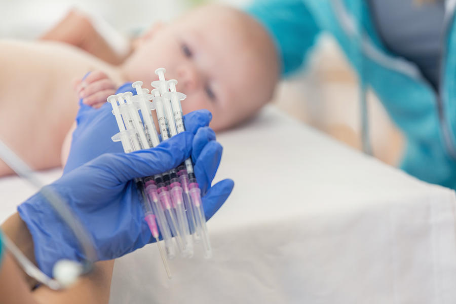 Pediatric nurse holds many syringes during babys well check appointment Photograph by SDI Productions