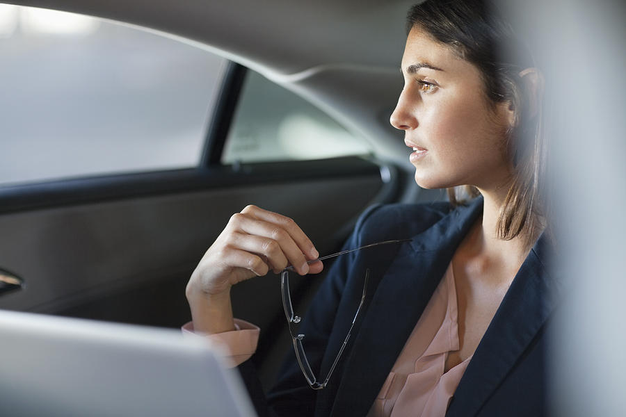 Pensive businesswoman with laptop in back seat of car Photograph by Sam Edwards