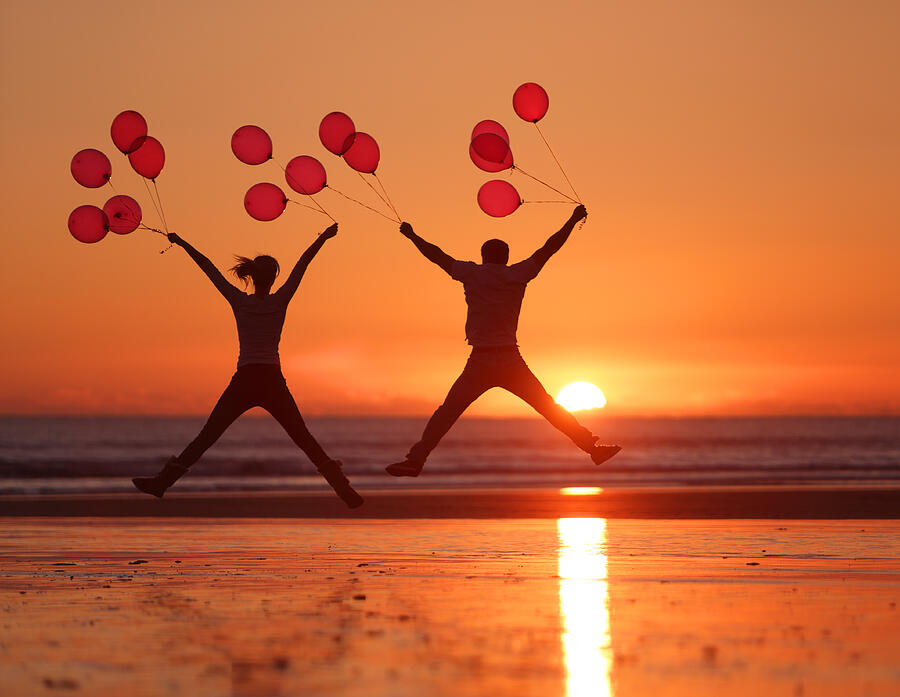 People jumping on beach at sunset holding balloons Photograph by Peter Cade
