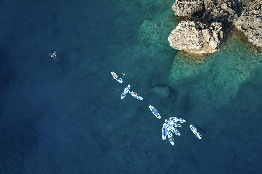 People kayaking and swimming in the idyllic blue sea  and rocky coastline. Photograph by Michalakis Ppalis