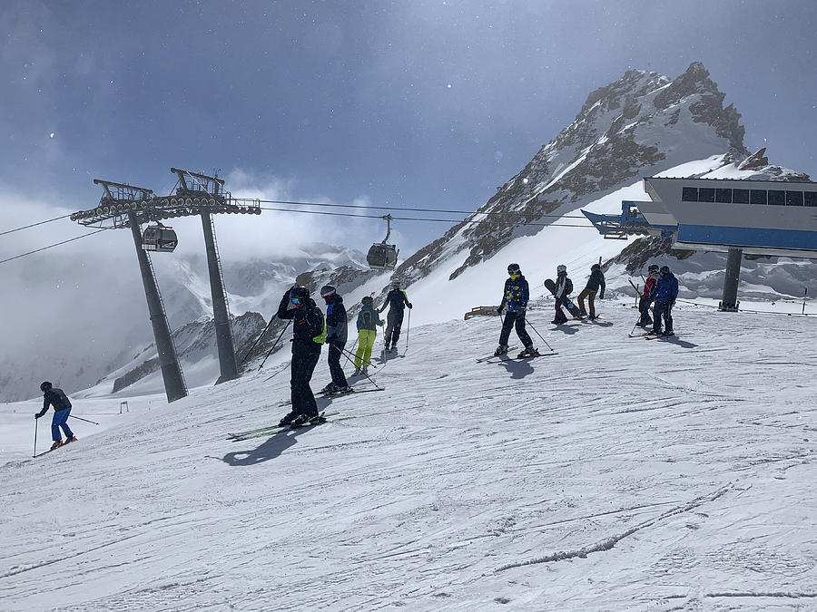 People preparing to ski and snowboard down a ski slope in the Sölden Ötztal ski area in the Austrian Alps during a sunny winter day. Photograph by Sjo
