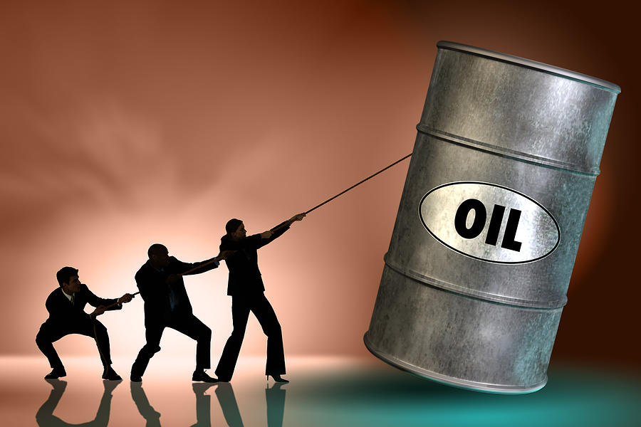 People tipping oil barrel Photograph by Comstock Images