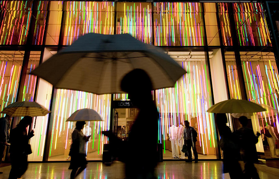 People walk past Louis Vuitton store in rain at night in Tokyo by Iain  Masterton