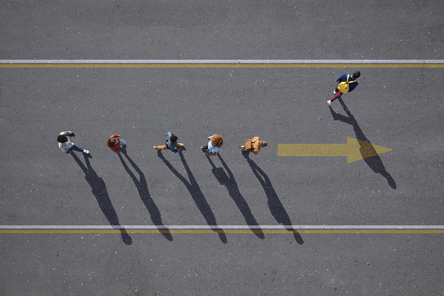 People walking in line on road, painted on asphalt, one person walking off. Photograph by Klaus Vedfelt
