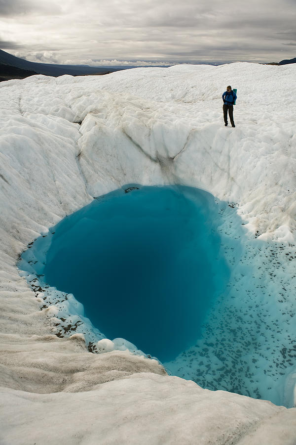 Person on glacier looking at  blue pool, McCarthy, Alaska. Photograph by Aurora Open