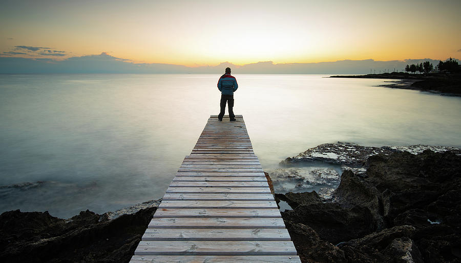 Person standing at the edge of a wooden pier in the sea at sunrise . People active outdoors enjoy ocean Photograph by Michalakis Ppalis