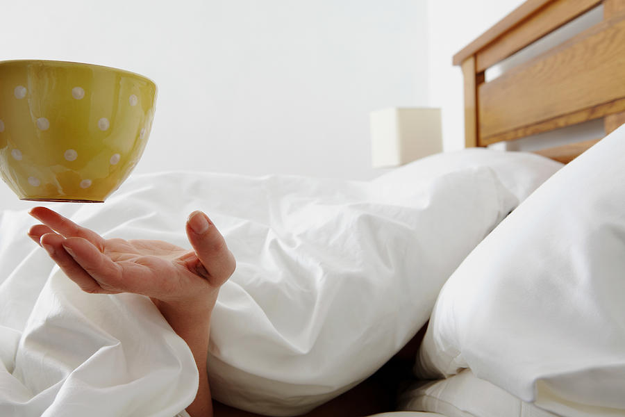 Person under duvet being handed a coffee Photograph by Image Source