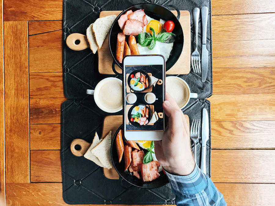 Personal perspective view of a young man taking picture with smart phone of a cafe table with breakfast served in skillets Photograph by Alexander Spatari