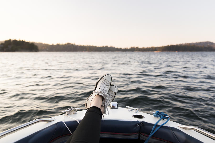 Personal perspective woman boating with feet up on tranquil lake Photograph by Caia Image