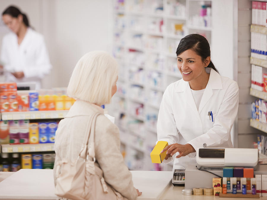 Pharmacist handing medication to customer in drug store Photograph by Tom Merton