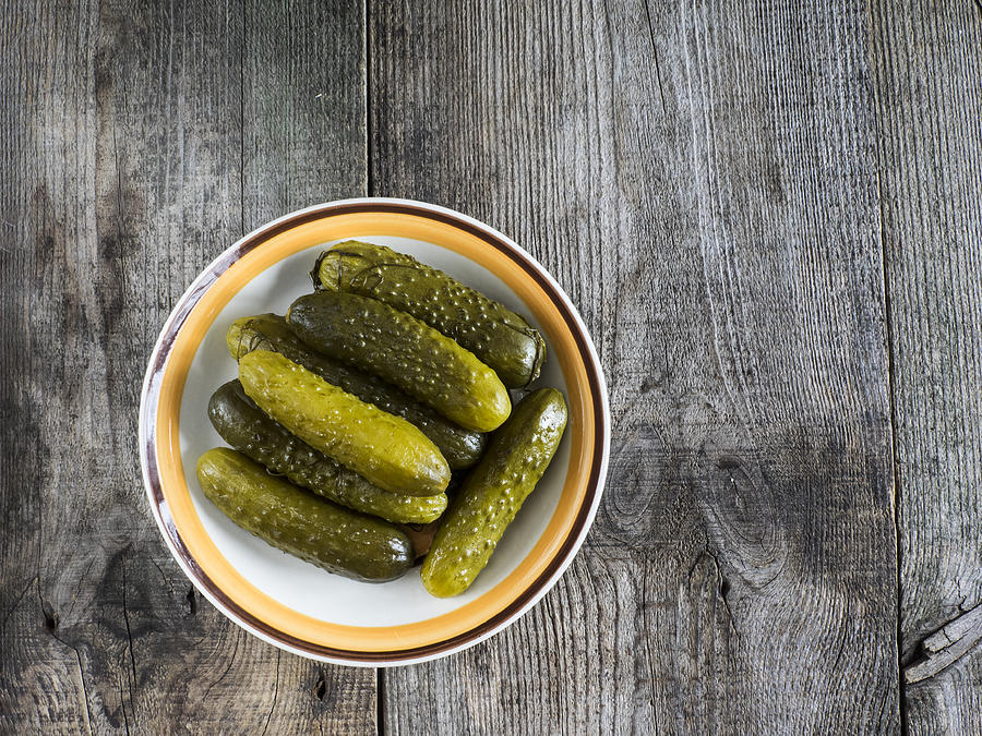 Pickled green gherkins in a bowl on a wooden table Photograph by IgorGolovnov
