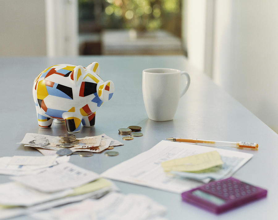 Piggybank, British Currency, Calculator, Receipts and a Mug on a Table Photograph by Digital Vision.