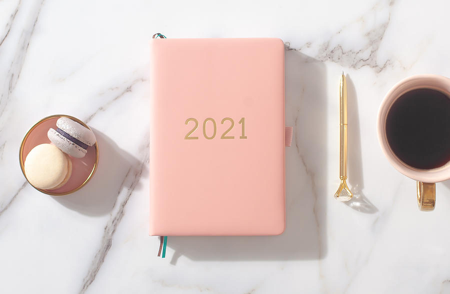 Pink coral colored diary for the year 2021, pen, coffee, macaron cookie. Marble background Photograph by Kostikova