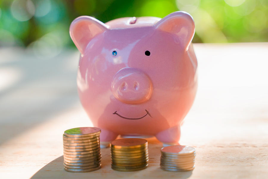 Pink piggy bank with some coins on the brown wooden table with the green background describes the concept of business, finance and money saving Photograph by Jantanee Phoolmas