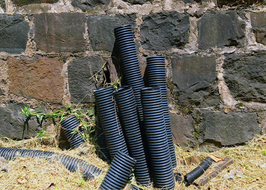 Pipes of power cables coming out of the ground on days of scorching sun next to a wall of stones. Photograph by CRMacedonio