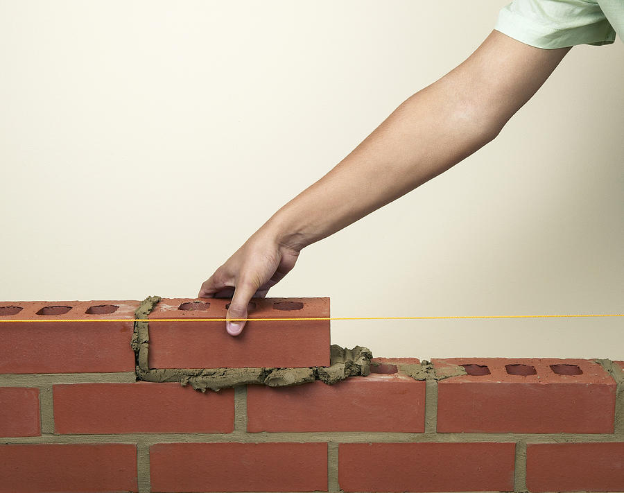 Placing a new brick on to fresh mortar on a wall Photograph by Dorling Kindersley
