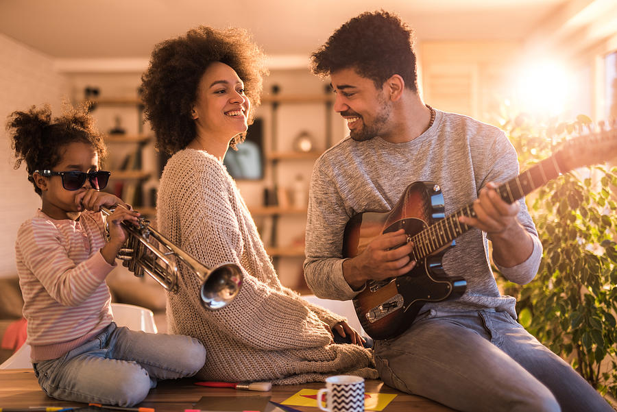 Playful black family having fun while playing musical instruments at home. Photograph by Skynesher
