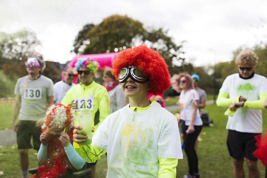 Playful boy runner in wig covered in holi powder at charity run in park Photograph by Caia Image
