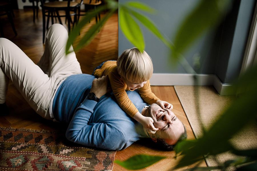 Playful daughter pinching cheerful fathers cheeks on floor at home Photograph by Maskot