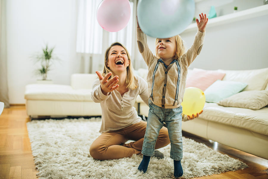 Playful mother and son having fun with balloons in the living room. Photograph by Skynesher