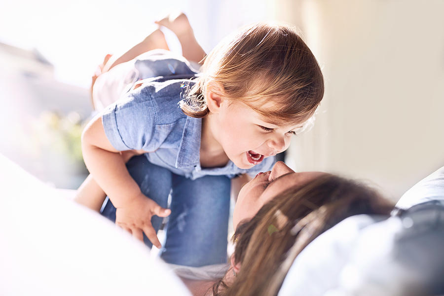 Playful mother holding laughing baby son on knees Photograph by Caia Image