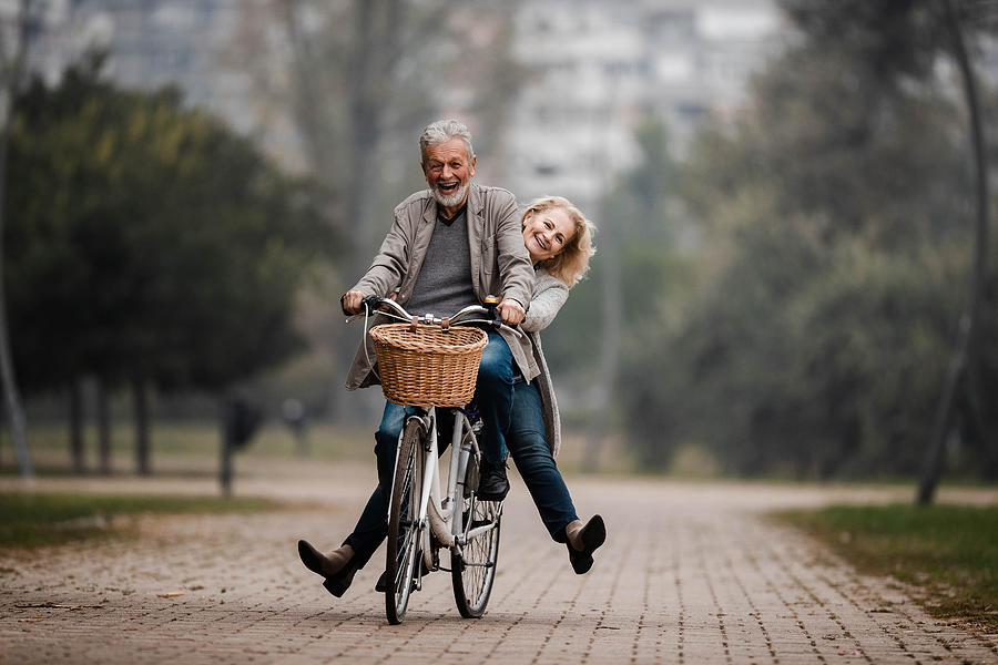 Playful senior couple having fun on a bike in autumn day. Photograph by Skynesher
