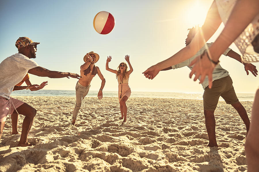 Playful young friends playing with beach ball on sunny summer beach Photograph by Caia Image
