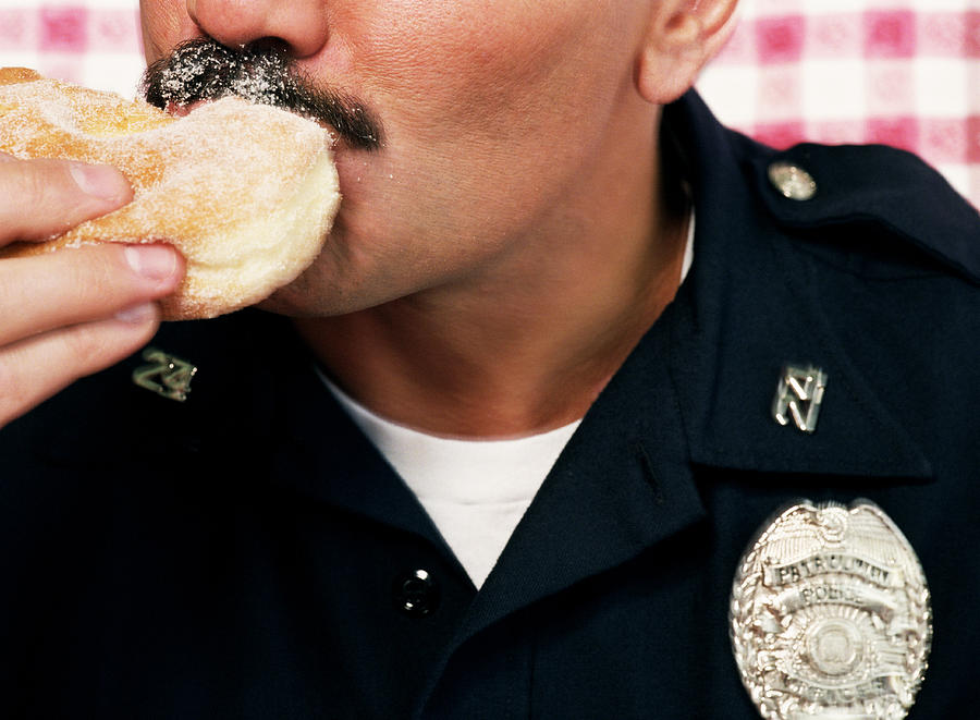 Policeman eating sugared doughnut, close-up Photograph by Sean Murphy