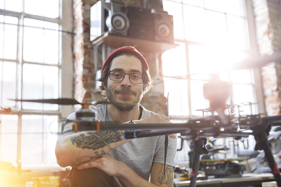 Portrait confident male designer with tattoos working on drone in workshop Photograph by Caia Image