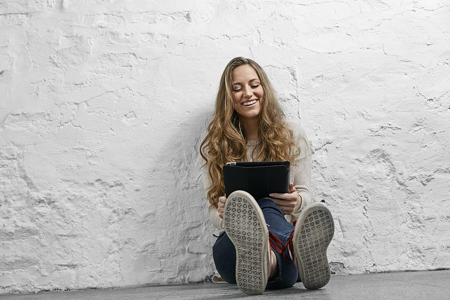 Portrait laughing young woman sitting on the floor using tablet Photograph by Westend61