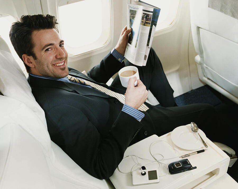 Portrait of a Businessman Sitting in a Plane Holding a Magazine and a Cup of Coffee Photograph by Digital Vision.