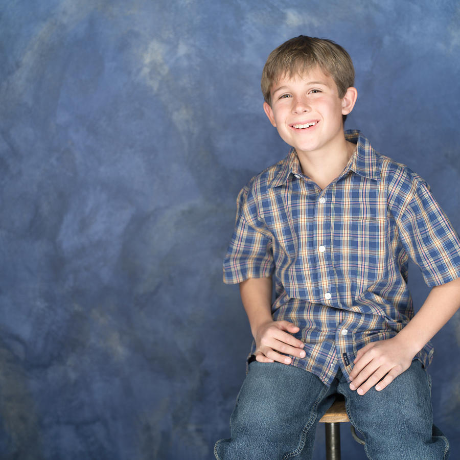 Portrait Of A Caucasian Boy In Jeans And A Plaid Shirt Rests His Hands On His Legs Looks Forward And Smiles Photograph by Photodisc