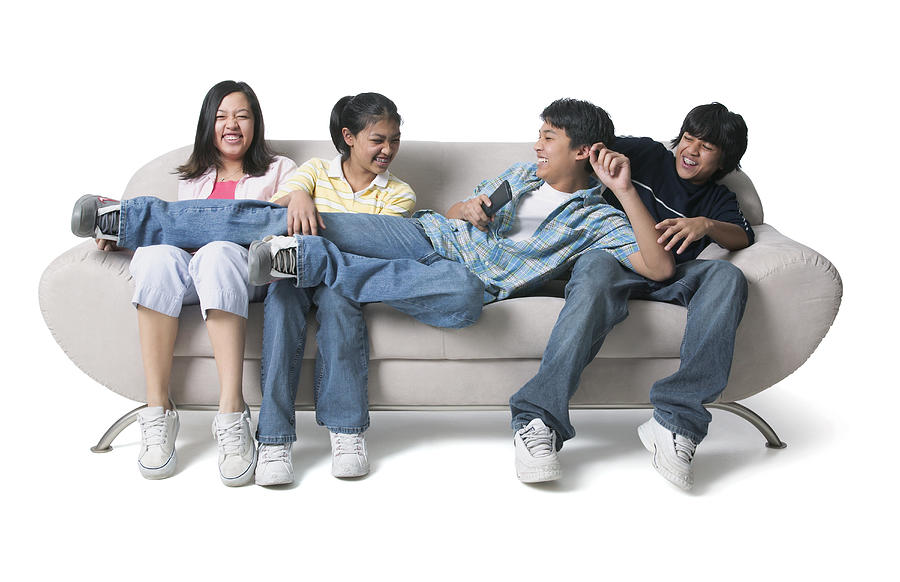 Portrait Of A Group Of Asian Brothers And Sisters As They Sit On The Couch And Fight Over The Remote Control Photograph by Photodisc