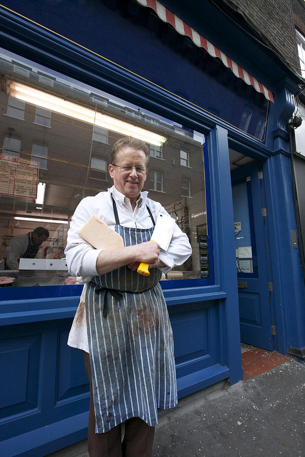 Portrait of a happy senior butcher standing outside shop with cleaver Photograph by Moodboard