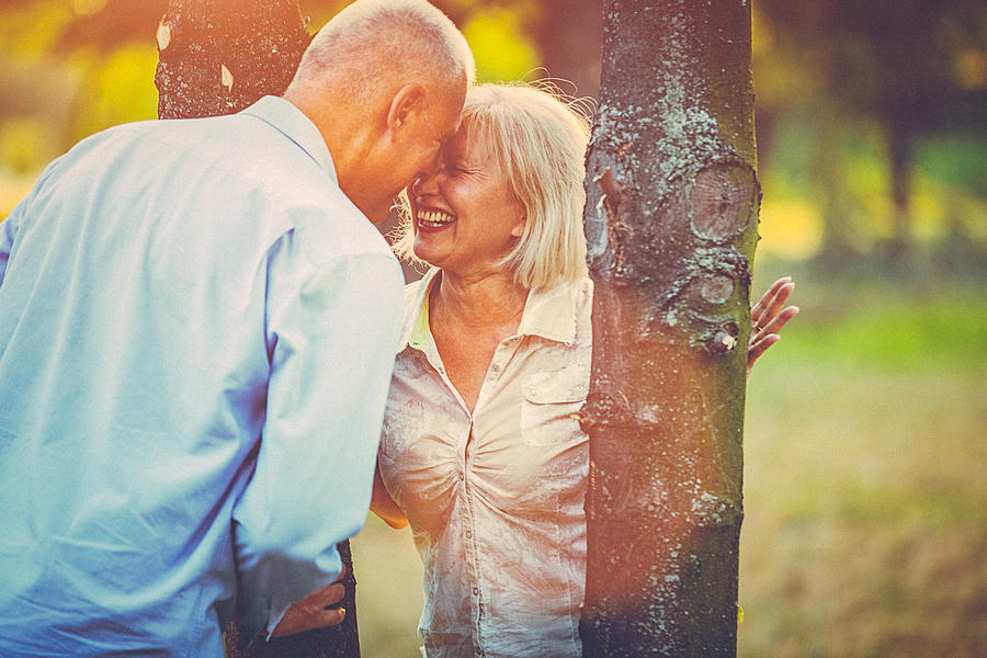 Portrait of a happy senior couple having fun, embracing and kissing in the public park at sunset Photograph by Gruizza