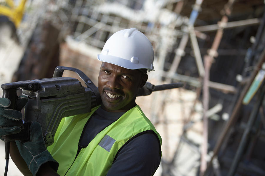 Portrait of a Male Builder in a Hard Hat, Carrying a Drill on His Shoulder Photograph by Digital Vision.