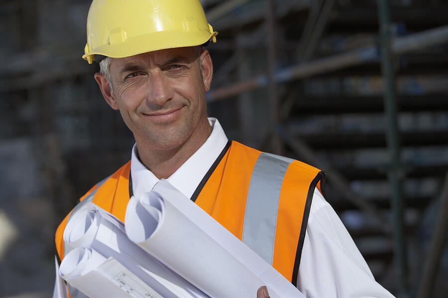 Portrait of a Man Wearing a Hard Hat and a Fluorescent Jacket, Holding Rolled Up Blueprints Photograph by Digital Vision.