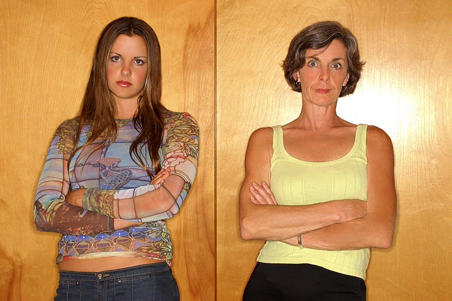 Portrait of a mother and daughter standing with arms crossed and looking angrily at the viewer. Photograph by Thinkstock