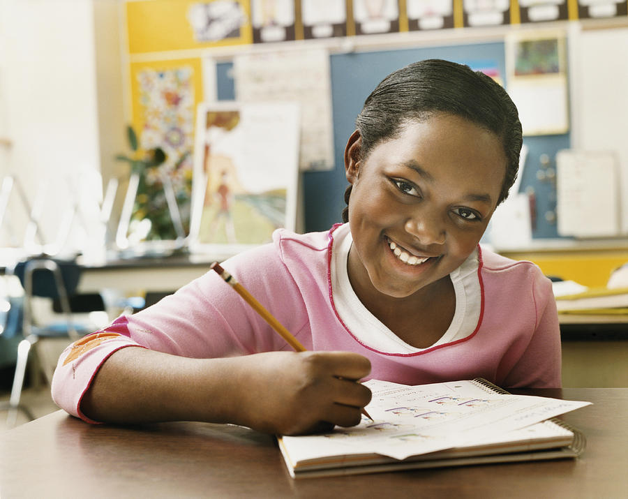 Portrait of a Schoolgirl Writing in Her Exercise Book in a Classroom Photograph by Digital Vision.