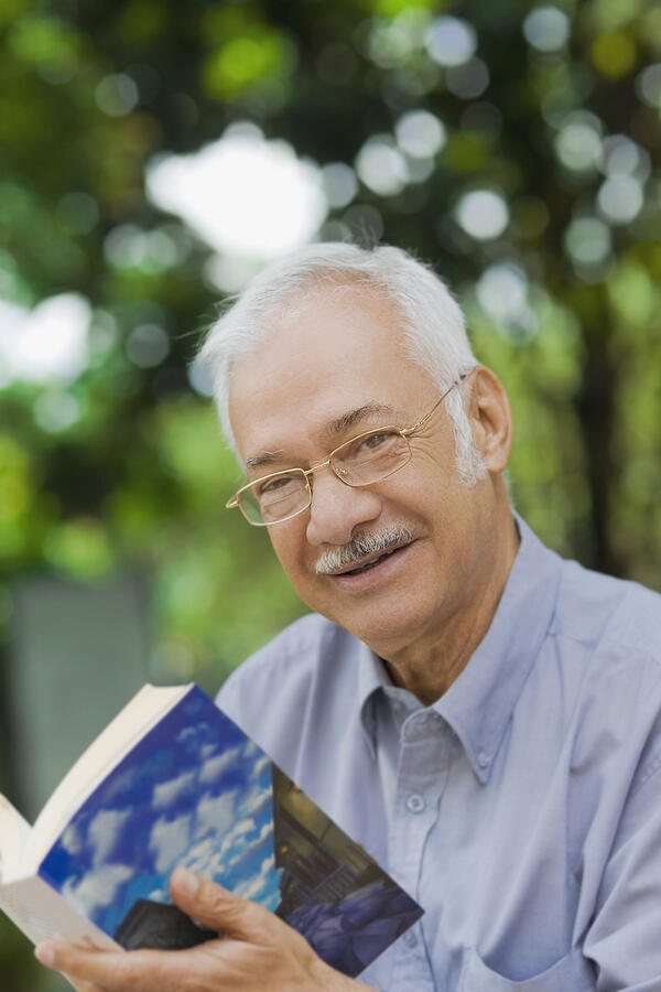 Portrait of a senior man holding a book and smiling Photograph by Glowimages