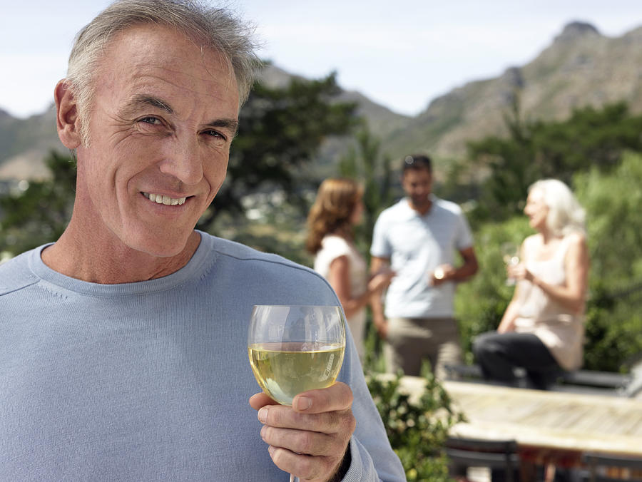 Portrait of a Senior Man With Glass of White Wine and a Group of People Standing Outdoors in the Background Photograph by Digital Vision.