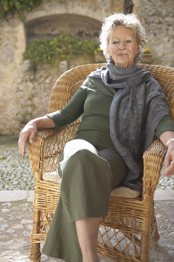 Portrait of a Senior Woman Sitting in a Wicker Armchair on a Terrace Photograph by Digital Vision.