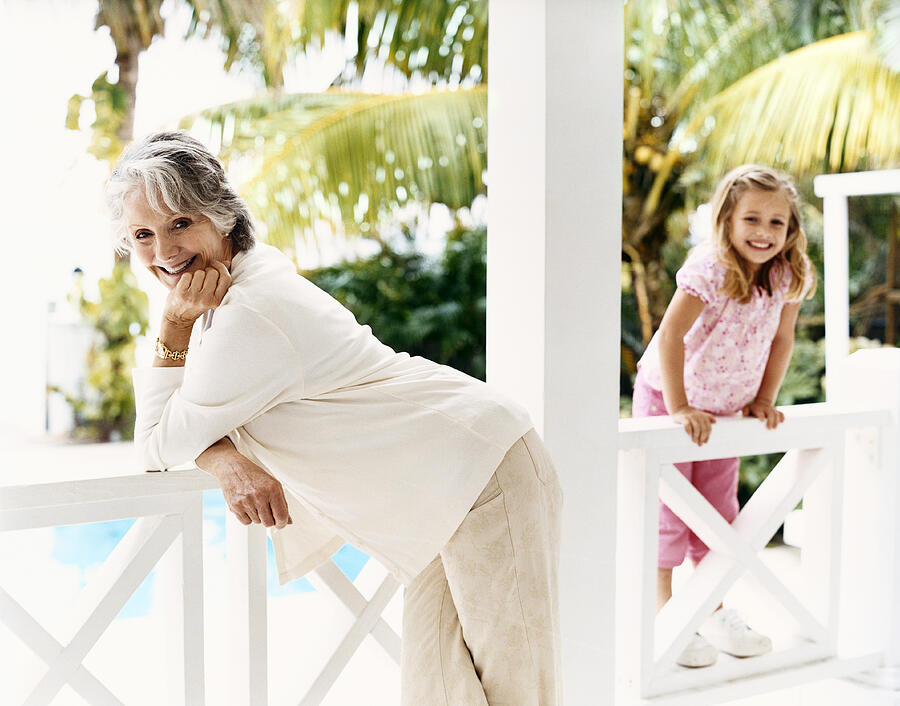 Portrait of a Senior Woman Standing on a Balcony With Her Young Granddaughter Photograph by Digital Vision.