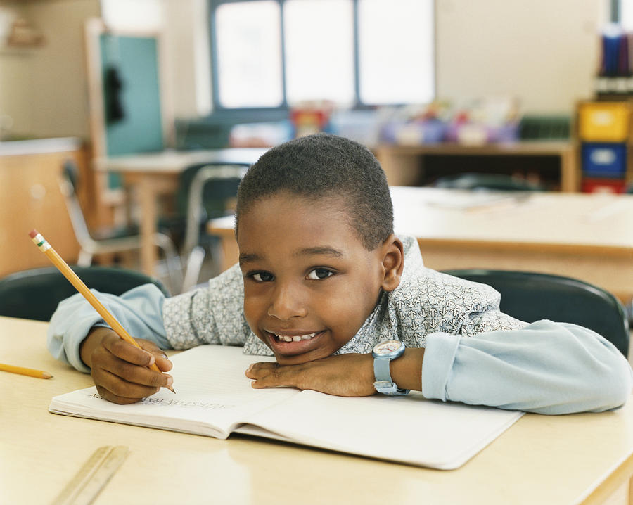 Portrait of a Smiling Schoolboy Sitting at a Table and Resting His Head on a Exercise Book Photograph by Digital Vision.