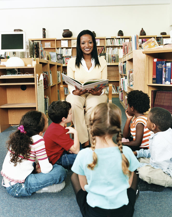 Portrait of a Teacher Reading a Story Book to Primary School Students in a Library Photograph by Digital Vision.