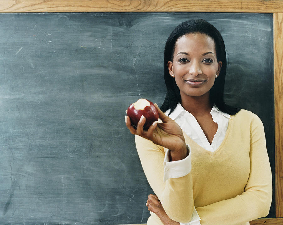 Portrait of a Teacher Standing in Front of a Blackboard Eating an Apple Photograph by Digital Vision.